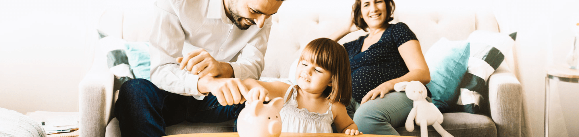 Little girl putting money in piggy bank with smiling parents in the background